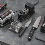 Bestcookhub - Various types of knife sharpeners (electric, whetstone, pull-through, honing rod) arranged on a kitchen counter with knives beside them